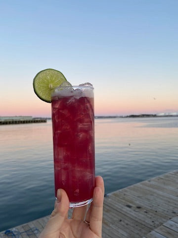 holding a cocktail on the dock in front of a sunset on the ocean