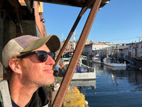 Ward Peck; wearing a baseball hat and sunglasses while looking out at the Portland harbor