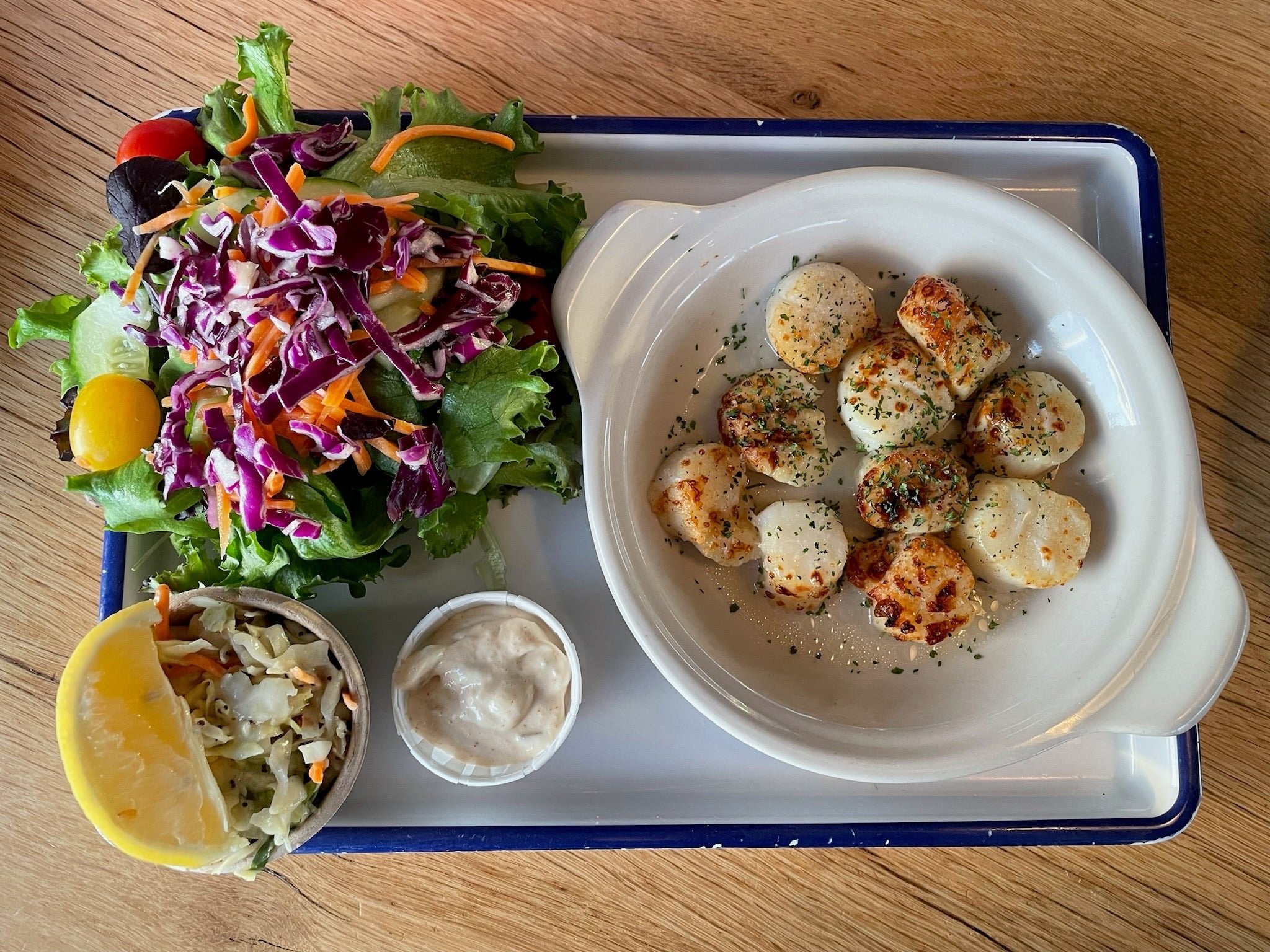 a tray with broiled scallops, a dish of salad, and slaw with a wedge of lemon