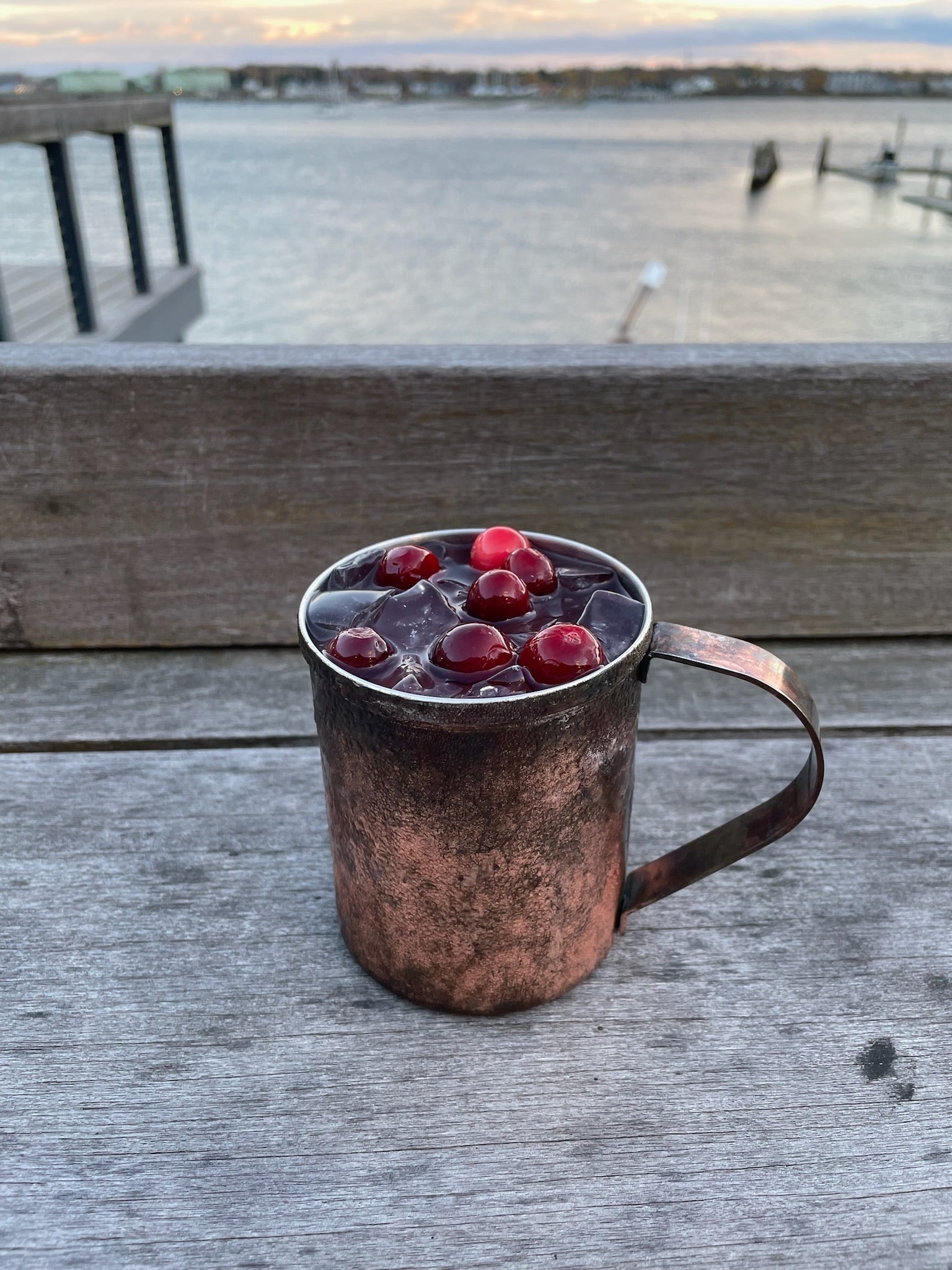 a cranberry cocktail in a mule glass on the deck in front of the ocean
