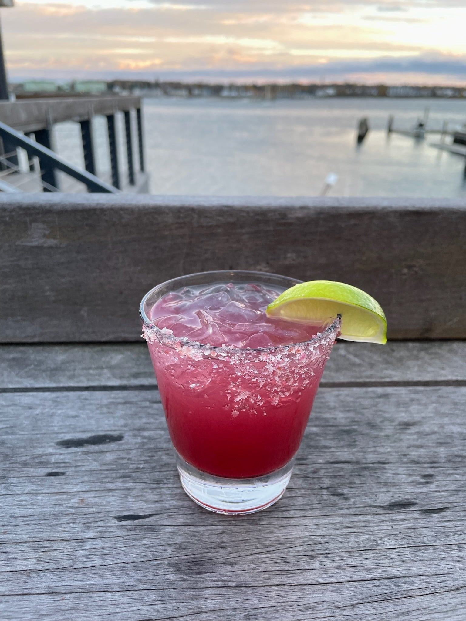 a margarita with a salted rim and a wedge of lime on the deck in front of the ocean