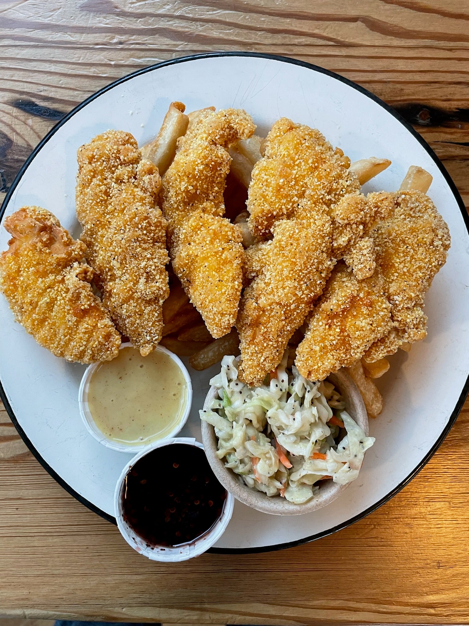 Fried chicken tenders over fries paired with sauce, a wedge of lemon, and slaw on a white plate