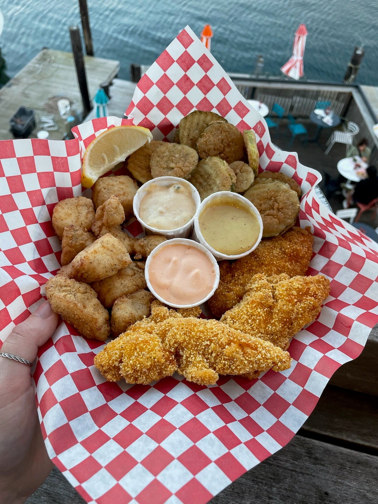 haddock bites, chicken tenders, fried pickles, and various sauces in a basket lined with wax paper