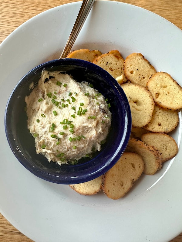 smoked pollock dip in a navy blue dish on a plate with bagel chips and a spoon