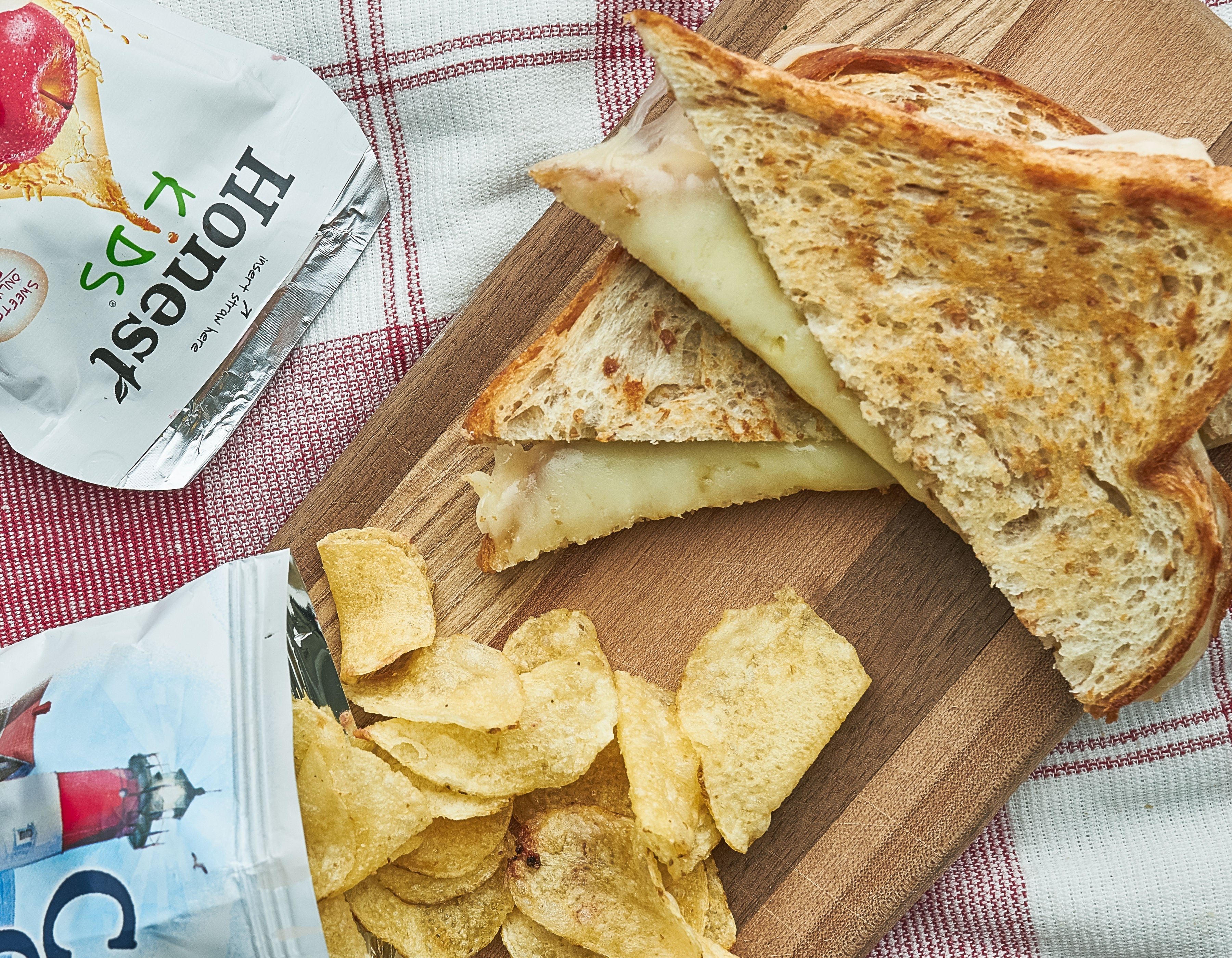 A grilled cheese, juice box, and bag of chips, on a plaid tablecloth