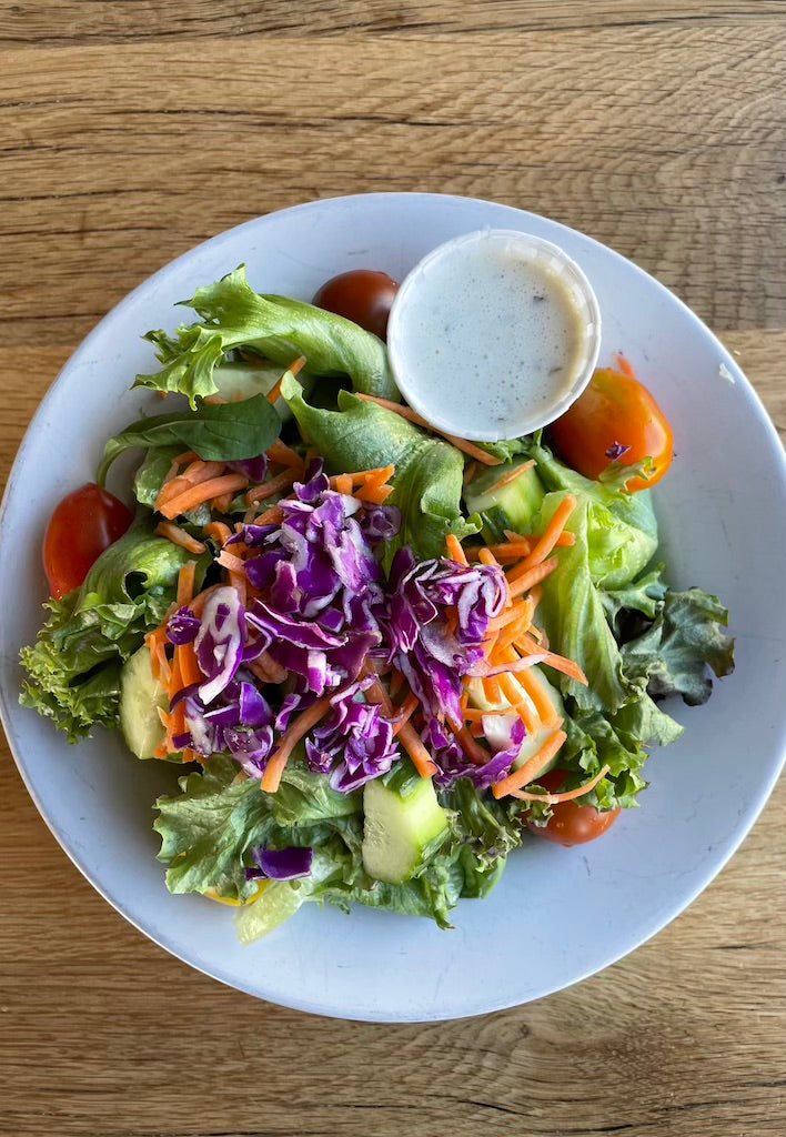 A bowl of salad with a side of dressing