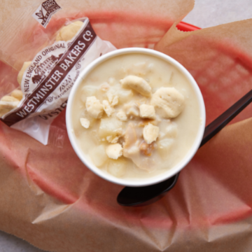 A cup of New England clam chowder and oyster crackers in a red basket lined with wax paper