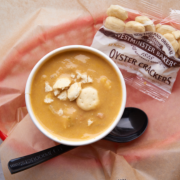 A cup of lobster bisque and oyster crackers in a red basket lined with wax paper